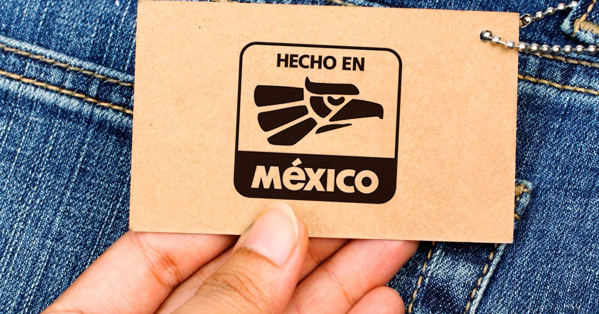 Etiqueta de cartón hecha en México en mano sobre fondo de mezclilla.