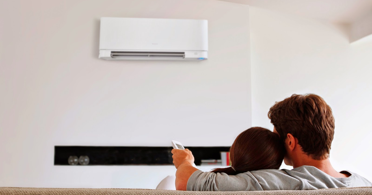 Pareja ajustando el aire acondicionado desde el sofá en un hogar moderno