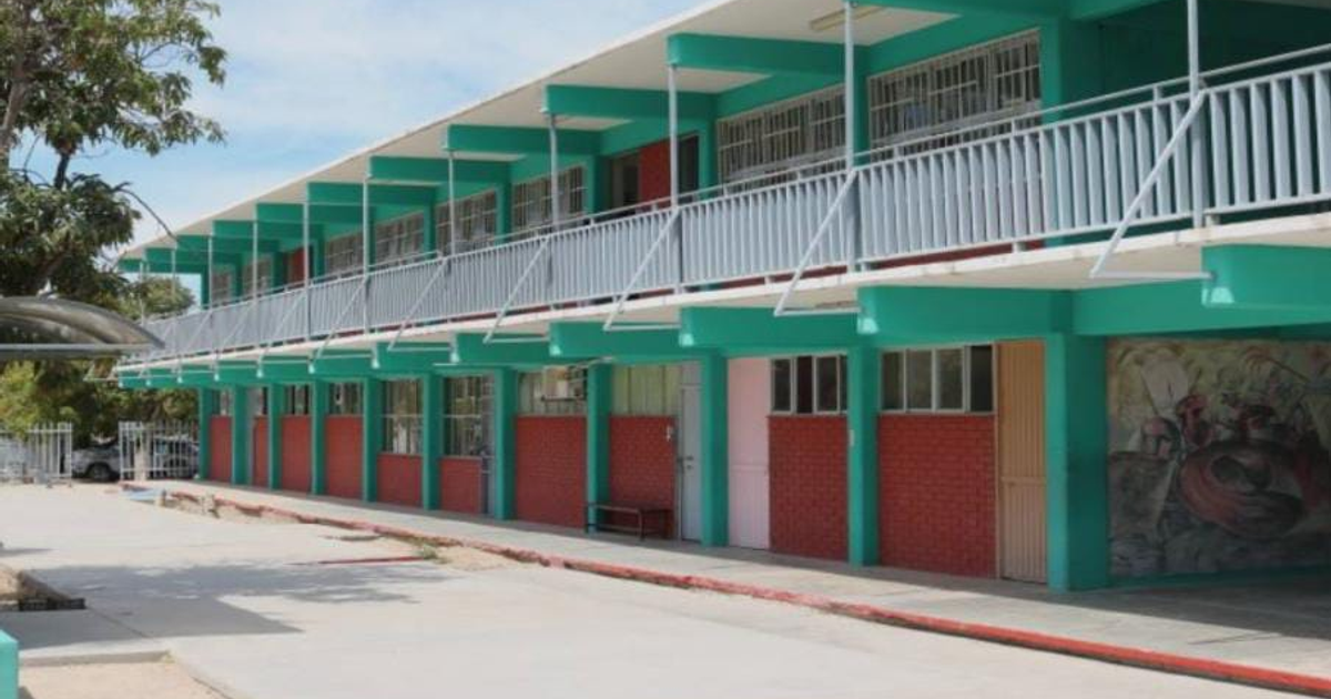 Edificio escolar moderno de dos plantas en Sinaloa con paredes verdes y rojas, balcones y áreas verdes al frente.