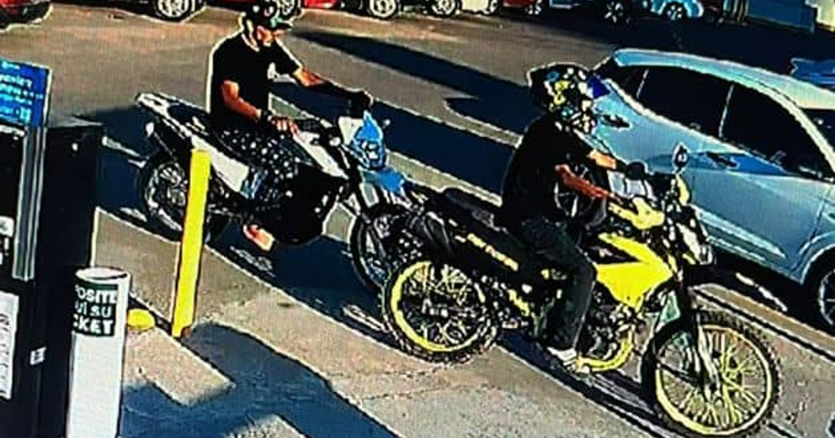 Dos motociclistas en estacionamiento; una moto es azul/blanca y otra amarilla/negra.
