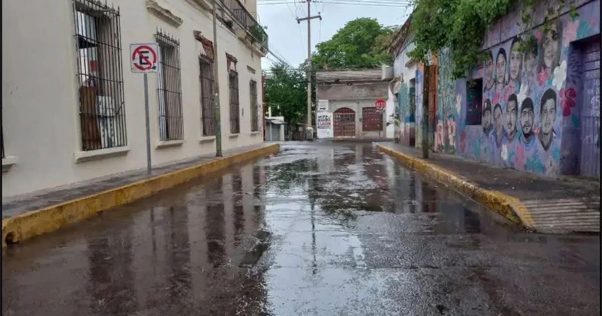 Calle mojada en Culiacán tras tormenta invernal, mostrando pavimento reflejante y edificios circundantes.