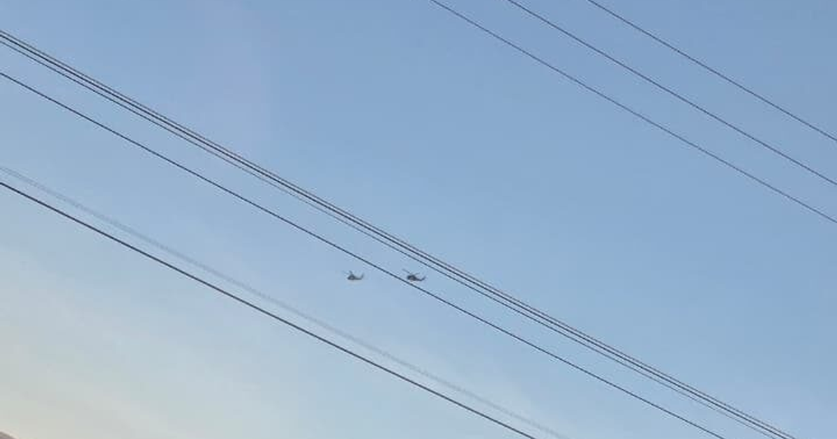 Dos helicópteros militares volando sobre Culiacán, con líneas eléctricas en el primer plano y un cielo despejado al fondo.
