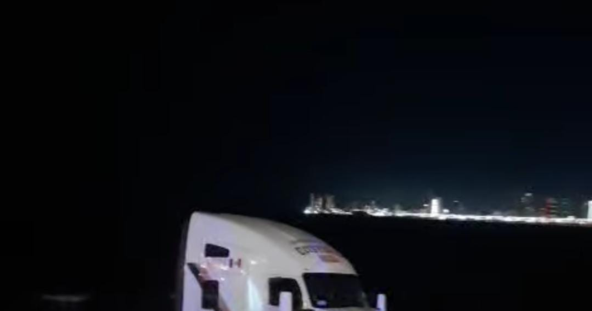 Camión estancado en la arena de Playa Norte con fondo urbano nocturno iluminado