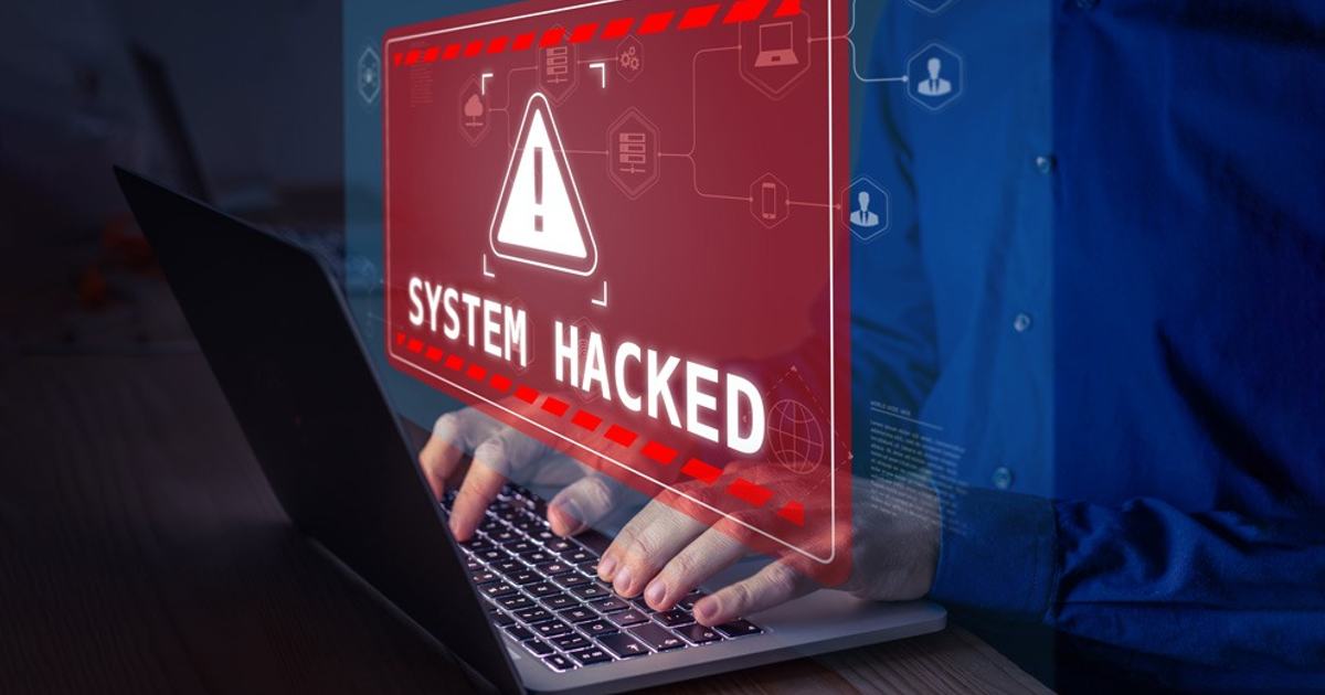 Mensaje de alerta 'SYSTEM HACKED' sobre fondo oscuro con figura usando laptop - Relacionado con el hackeo en UNAM.