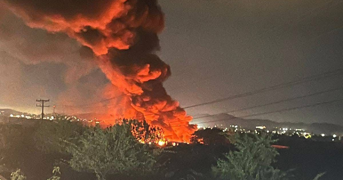 Incendio nocturno en Villa Unión con llamas y humo, árboles y luces de ciudad en el fondo.