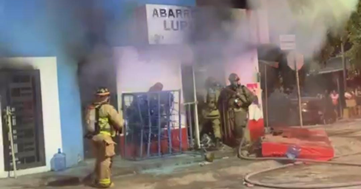 Bomberos combatiendo incendio en 'Abarrotes Lupita' con pobladores mirando en Culiacán.