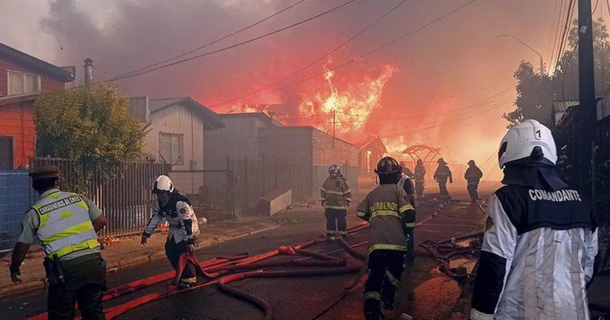 Bomberos combaten incendio en región urbana de Chile con casas afectadas al fondo